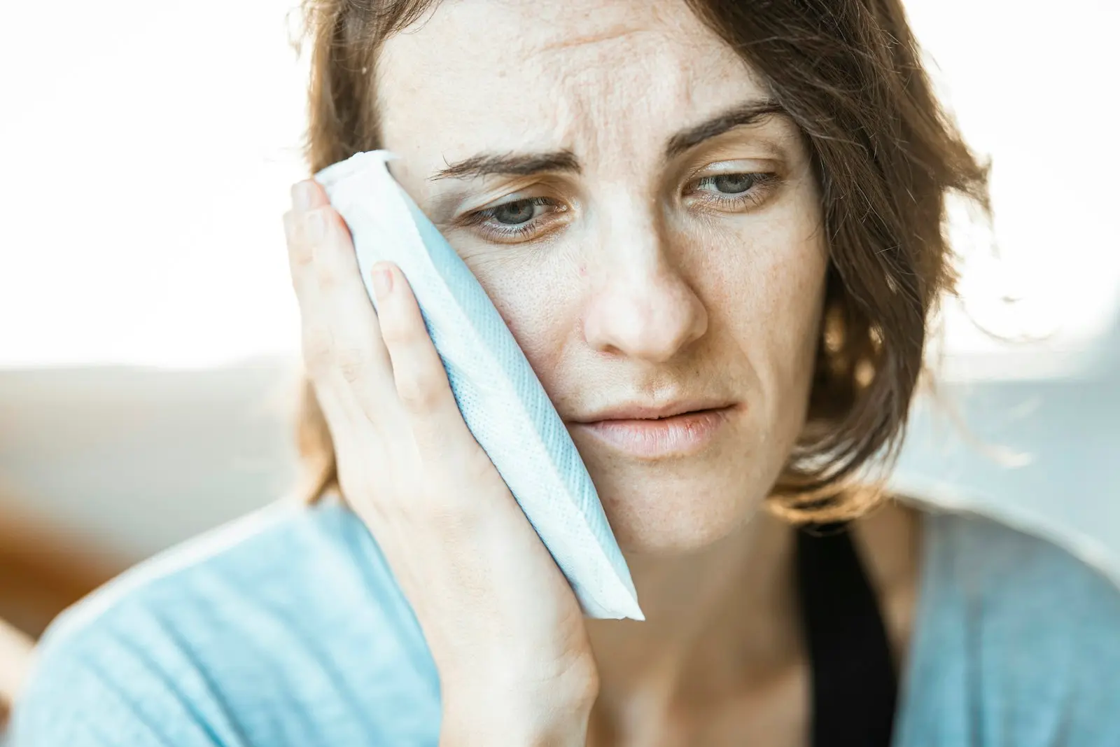 Woman holding an ice pack to her cheek with a toothache — emergency dental care at London Square Dental Calgary